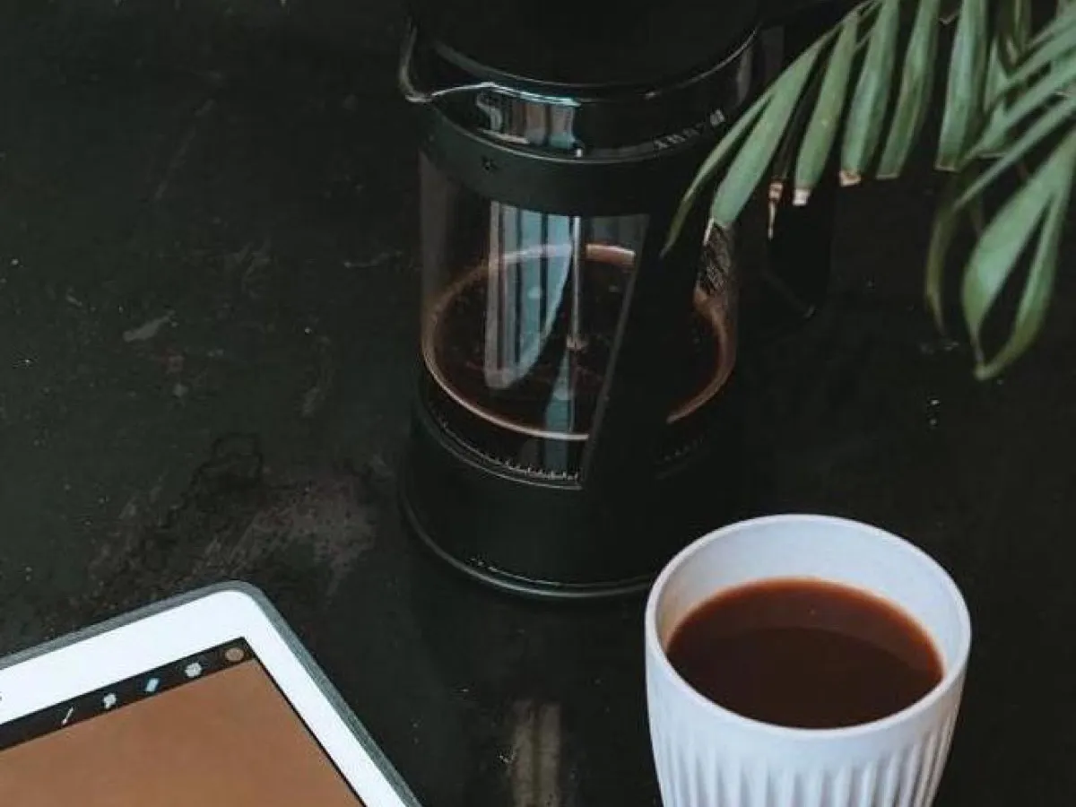 Cafetière à piston remplie de café et tasse blanche sur une table sombre