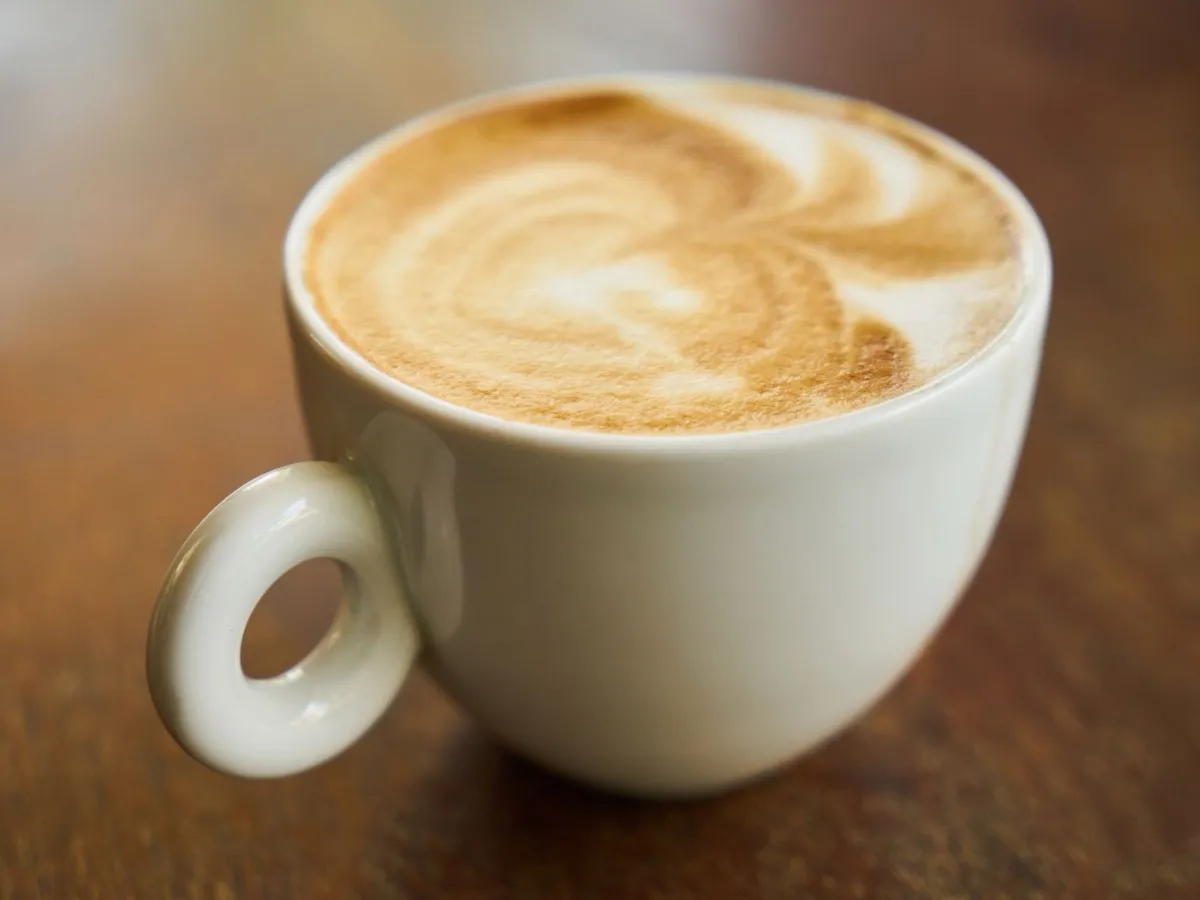 Cappuccino à la mousse crémeuse et latte art dans une tasse blanche posée sur du bois