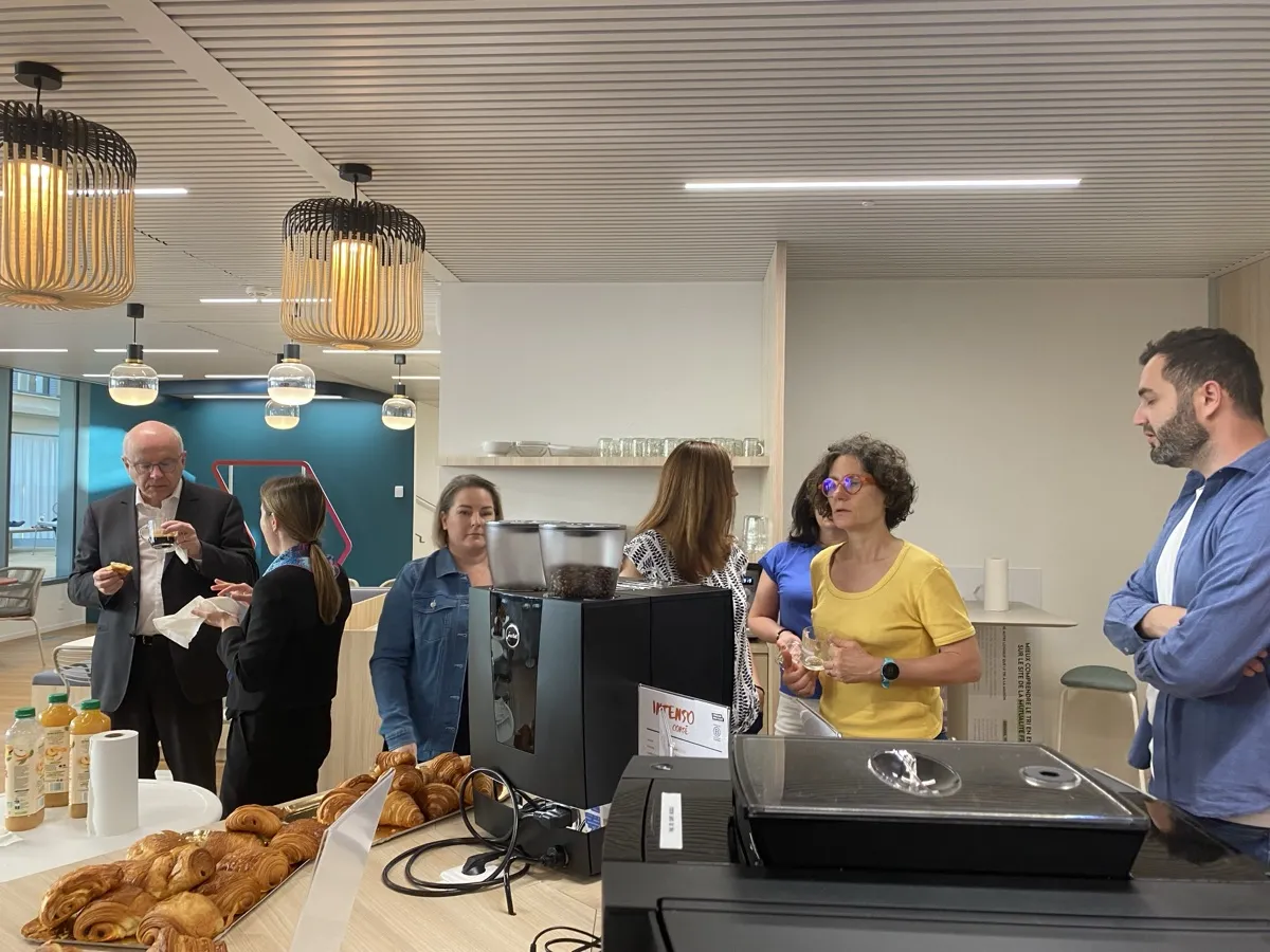 Collègues en pause café autour d'une machine à grains et de viennoiseries dans un espace d'entreprise