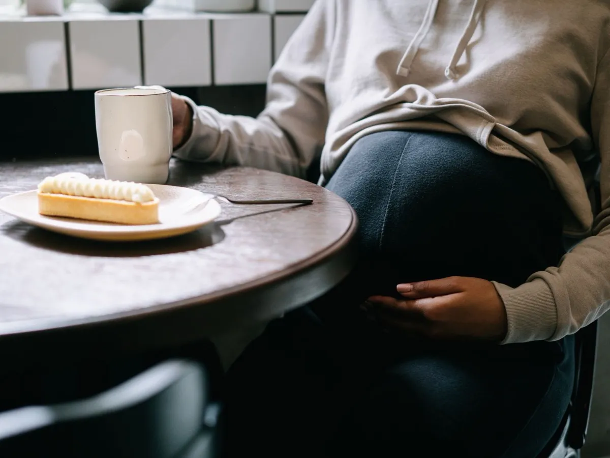 Femme enceinte attablée tenant une tasse de café, question du café pendant la grossesse