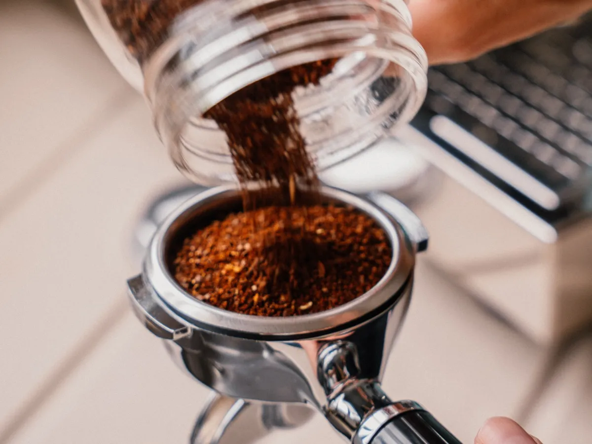 Main versant du café moulu dans le porte-filtre chromé d'une machine à expresso