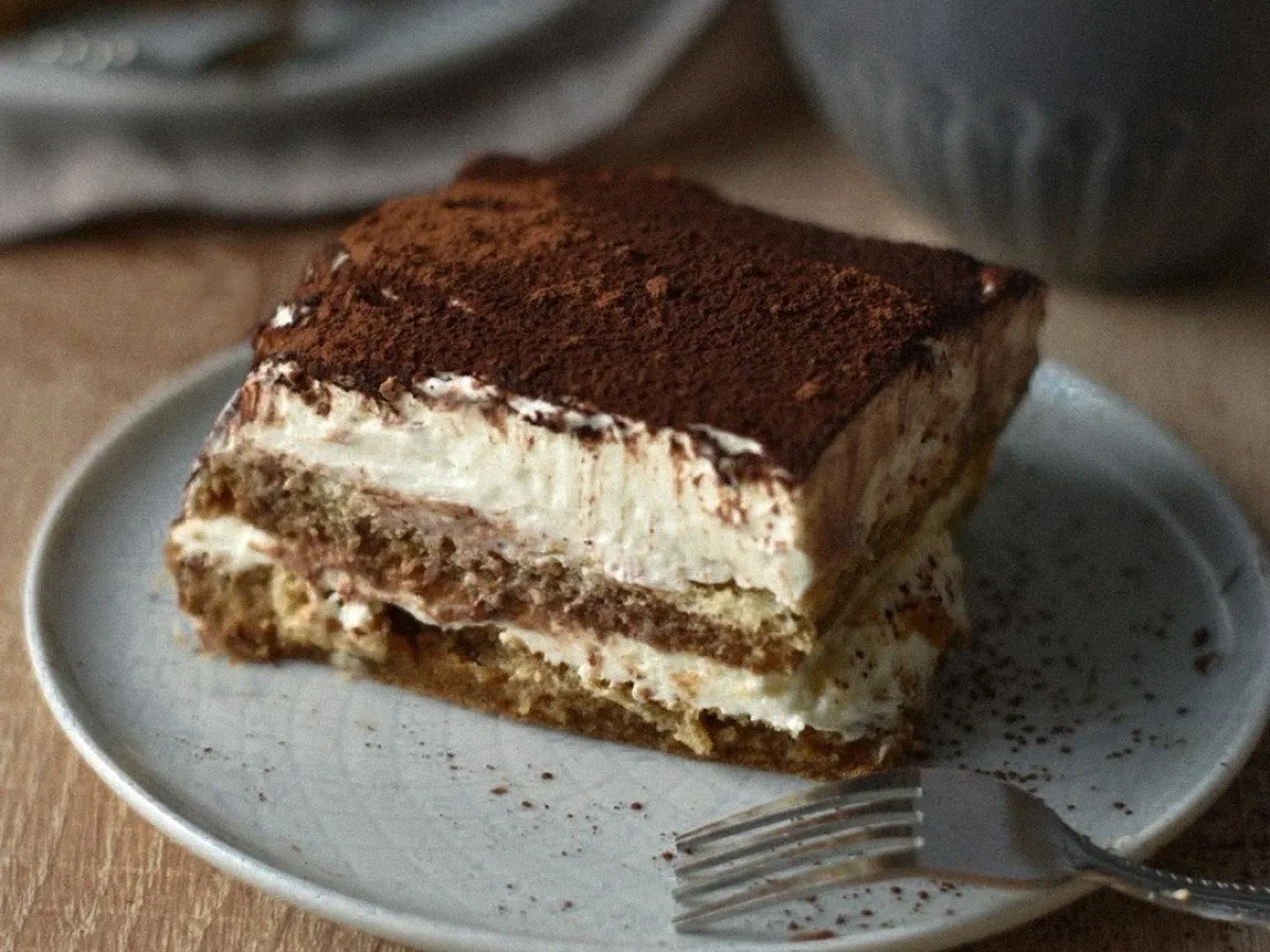 Part de tiramisu au café aux couches crémeuses saupoudrée de cacao, près d'une tasse de café